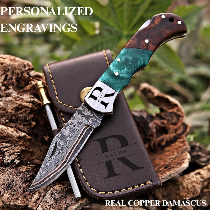 Copper Damascus folding knife with green and wood handle on an engraved leather sheath